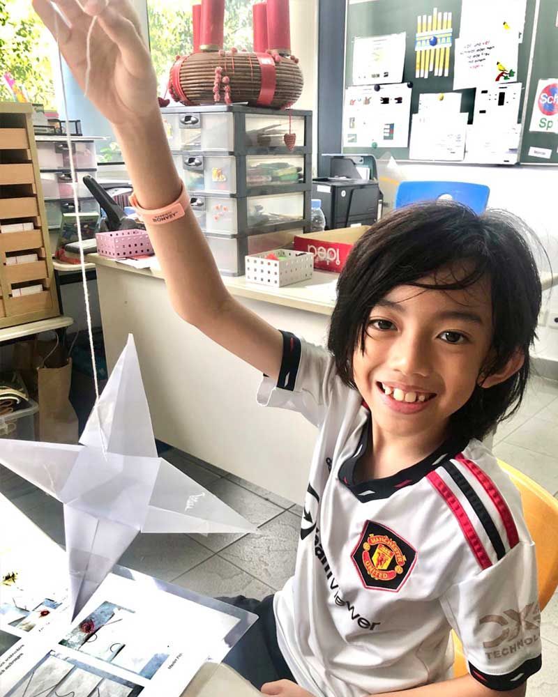A young boy is sitting at a table with his arm in the air.