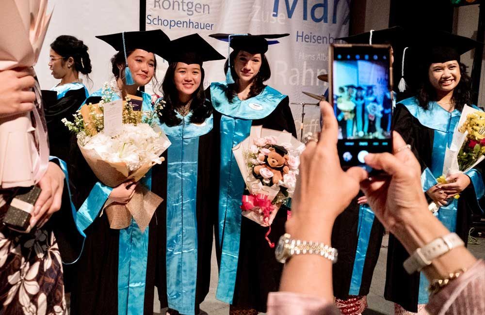 A woman is taking a picture of a group of graduates holding bouquets of flowers.