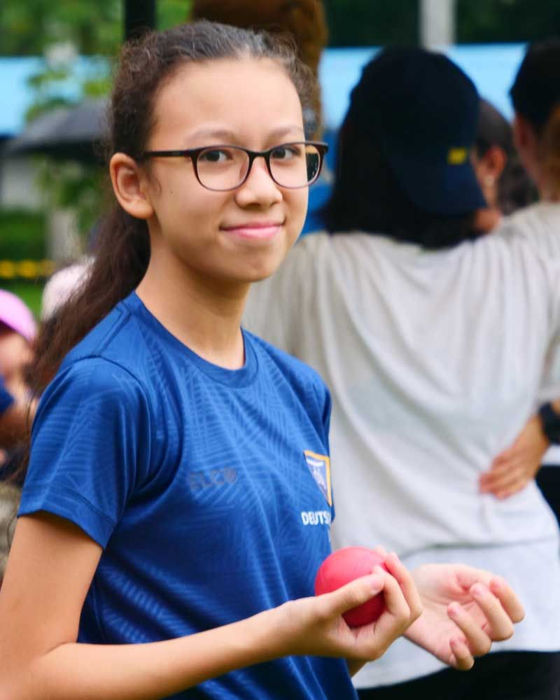 A girl wearing glasses and a blue shirt is holding a red ball.