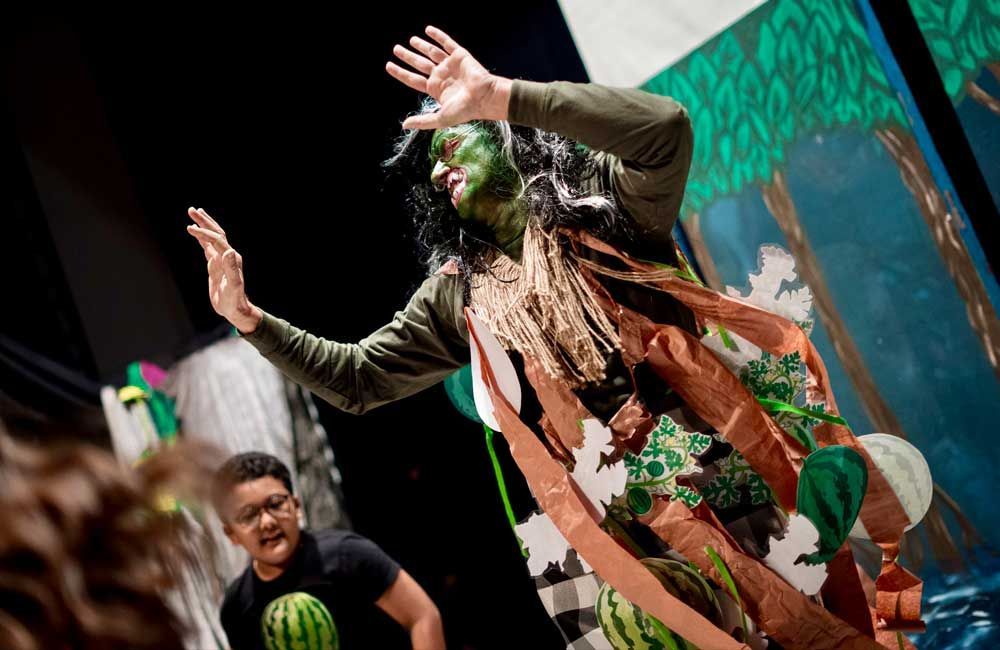 A man in a black shirt with a watermelon on it is standing next to a man in a green costume.