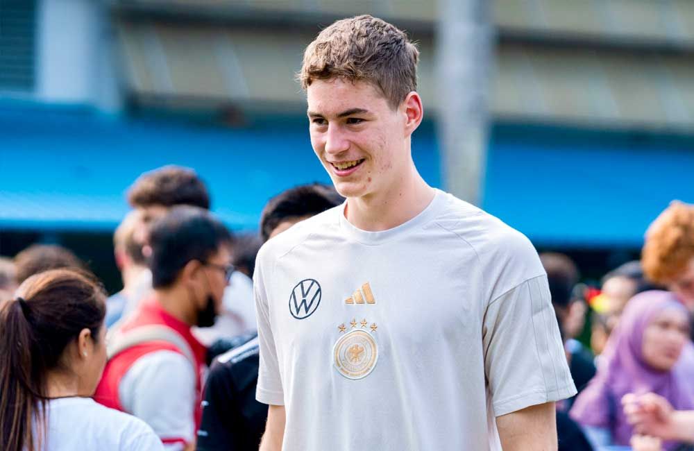 A young man wearing a white adidas shirt is standing in a crowd of people.