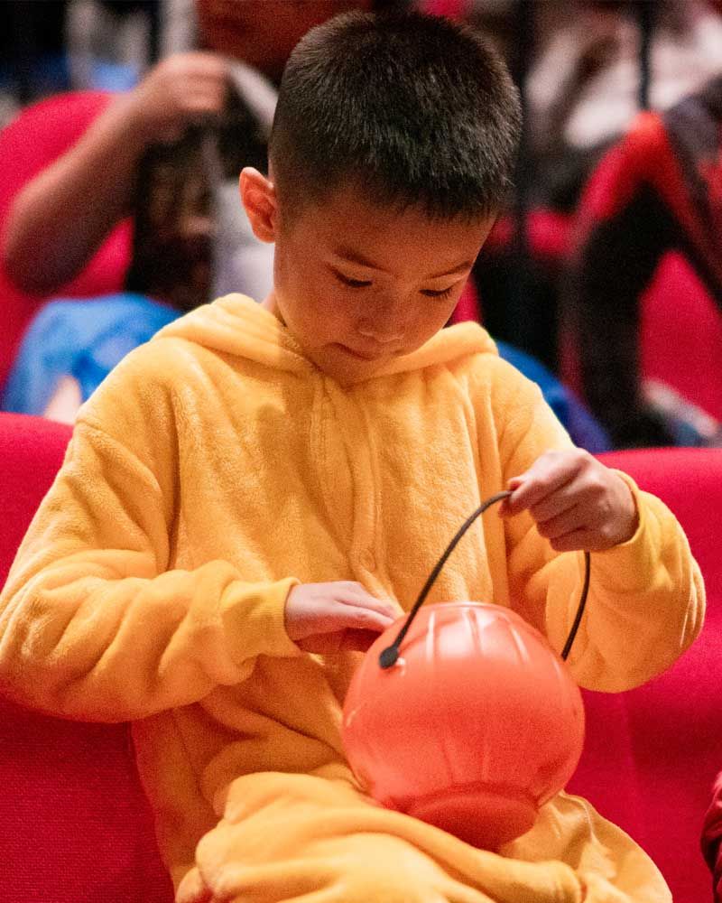 A young boy in a winnie the pooh costume is holding a trick or treat bucket.