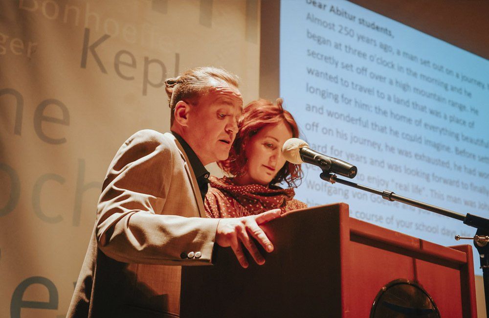 A man and a woman are standing at a podium talking into microphones.