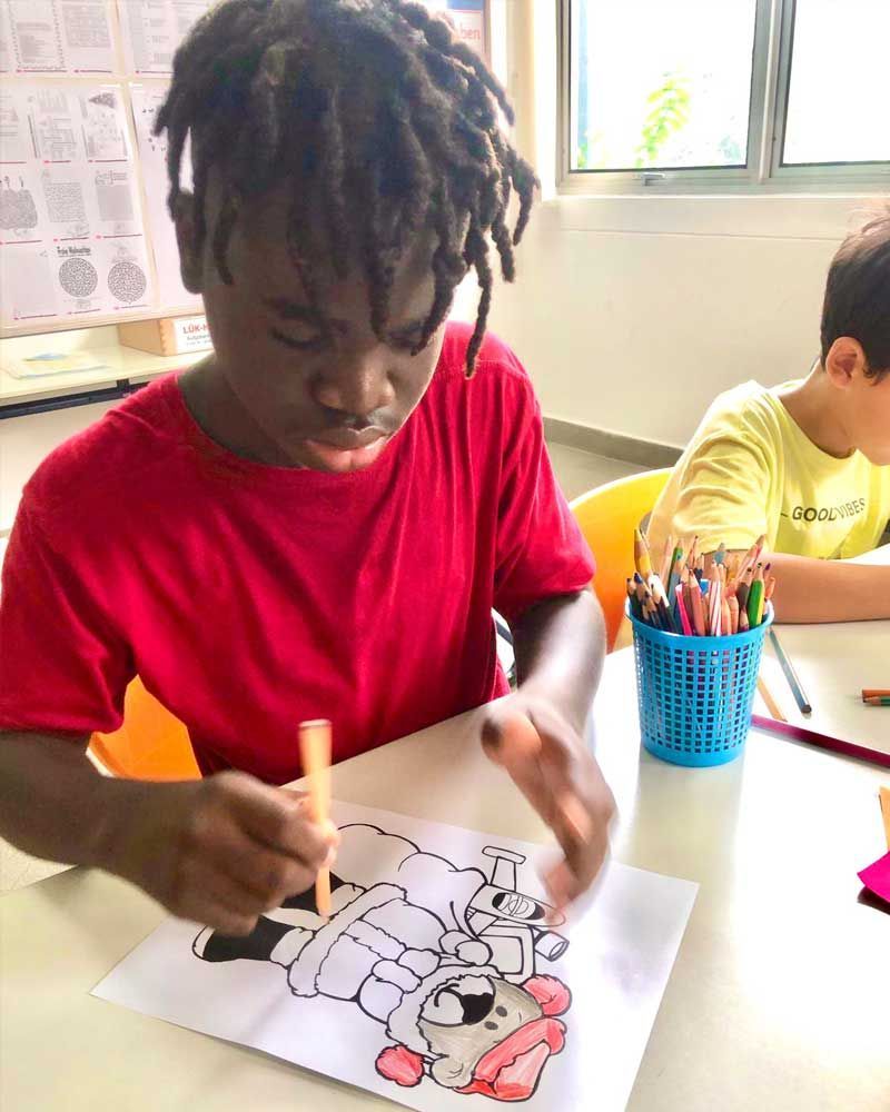 A young boy is sitting at a table drawing a picture of a dog.