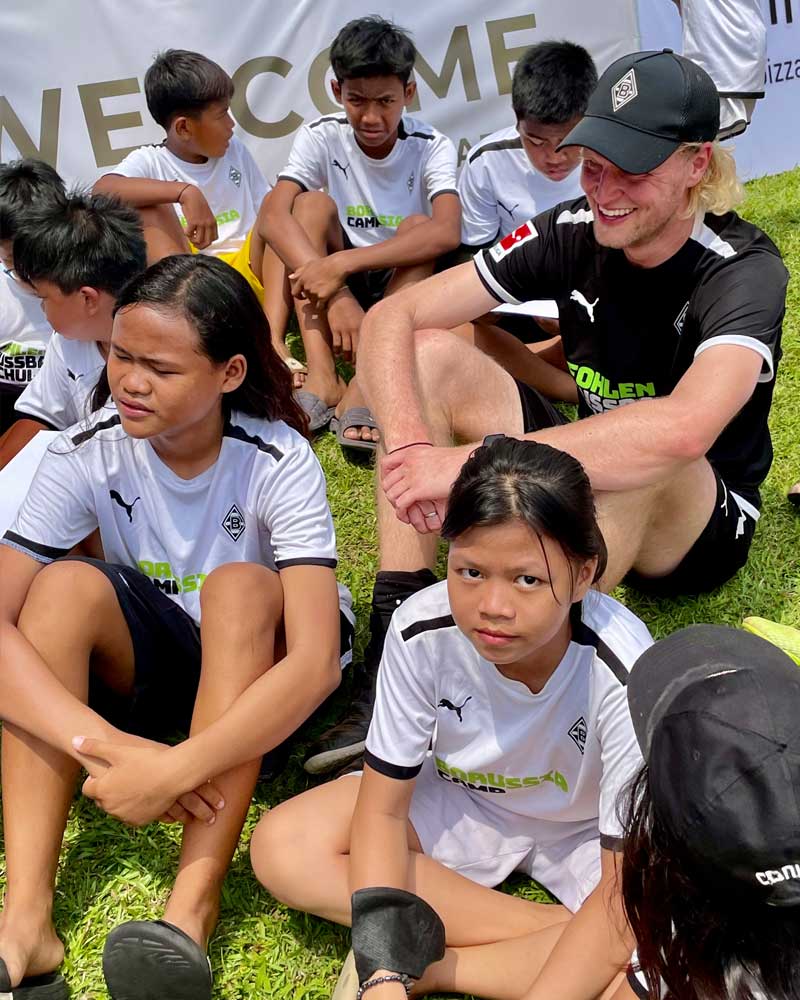 A group of children are sitting on the grass with a man sitting next to them.
