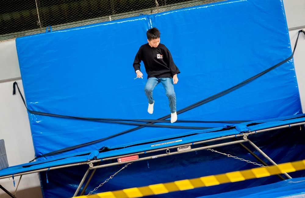 A young boy is jumping on a blue trampoline.