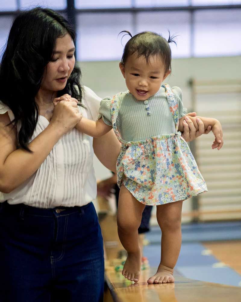 A woman is helping a baby walk on a balance beam.