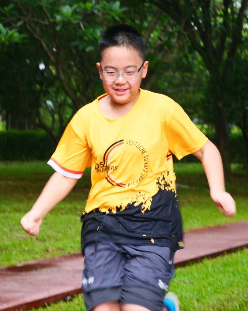 A young boy wearing a yellow shirt and black shorts is running in a park