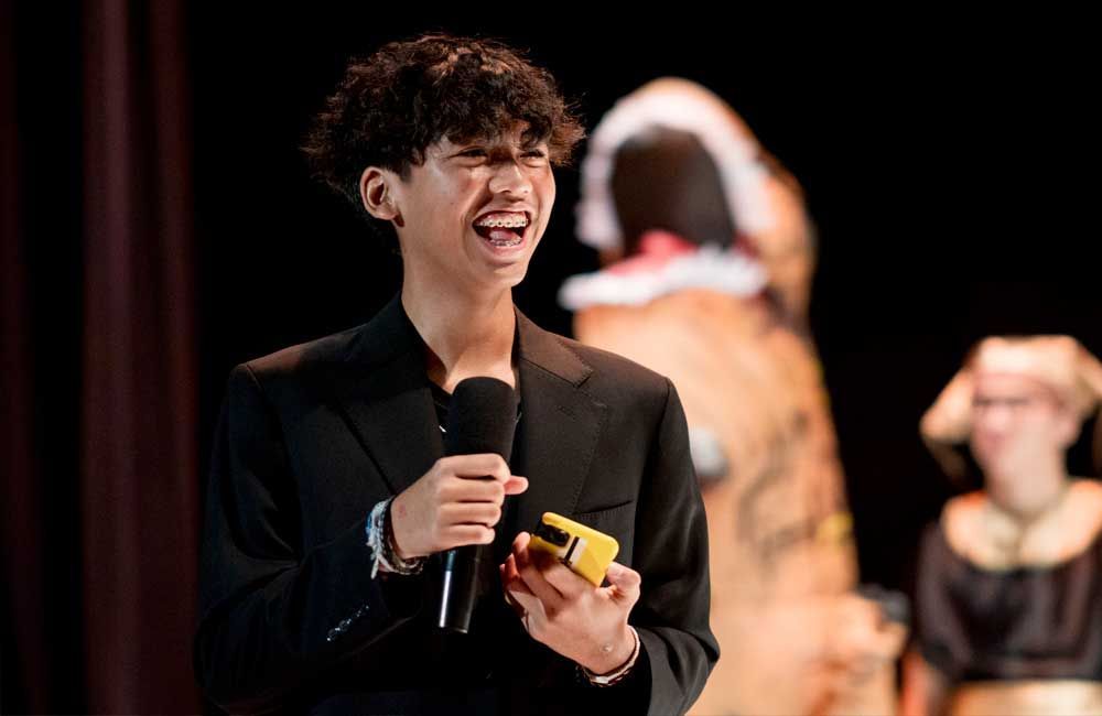 A man in a suit is holding a microphone in front of a dinosaur costume.