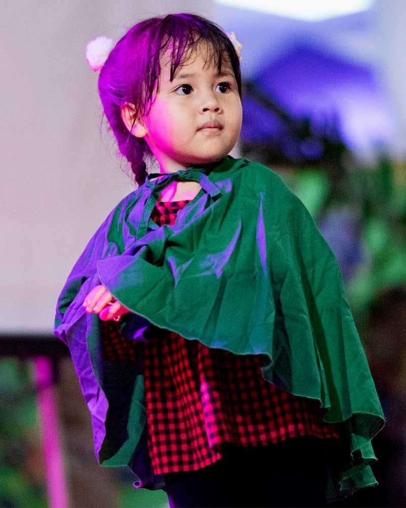A little girl wearing a green cape and a red dress