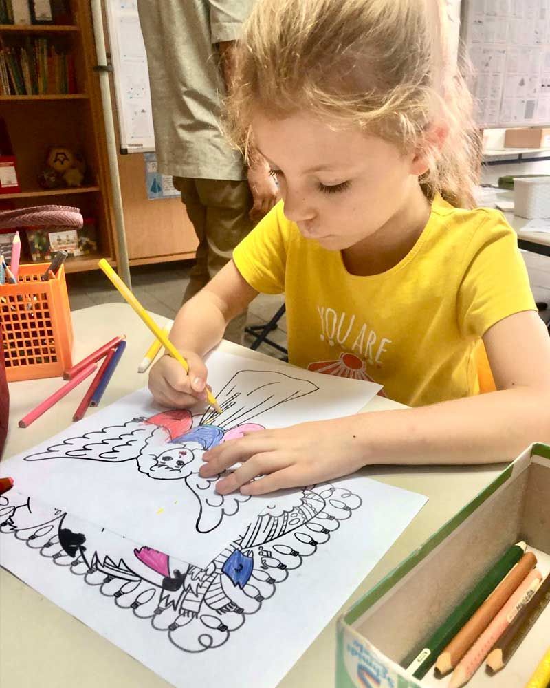 A little girl is sitting at a table drawing with colored pencils.