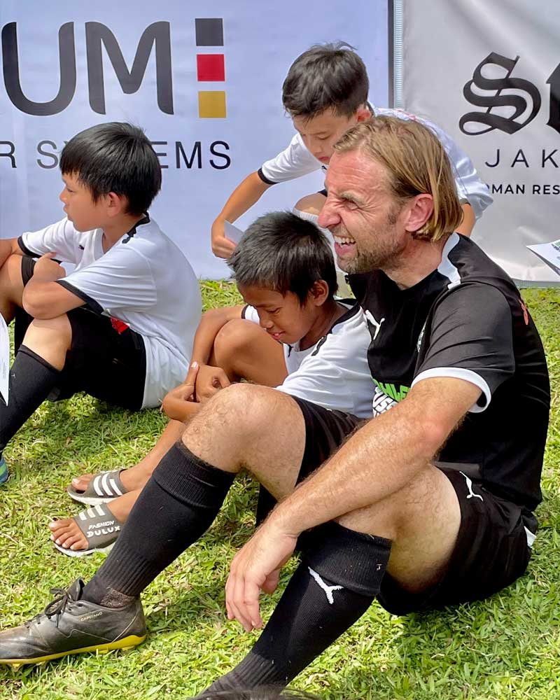 A group of young boys are sitting on the grass with a man.