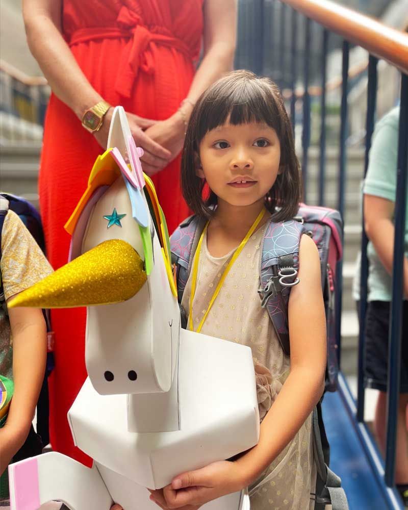 A little girl is holding a unicorn made out of cardboard