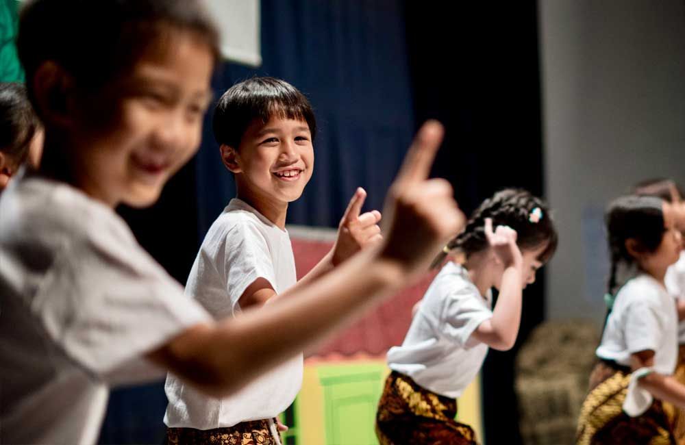 A group of children are dancing on a stage and one of them is giving a thumbs up.