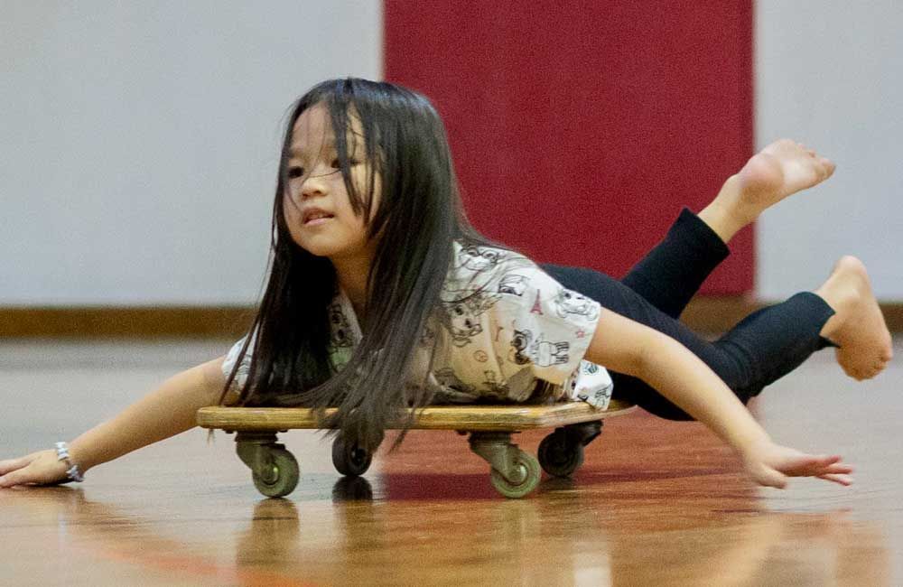 A little girl is rolling on a wooden skateboard on a wooden floor.