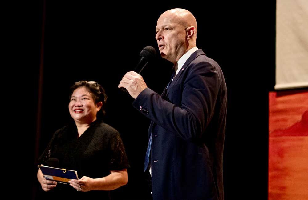 A man and a woman are standing on a stage holding microphones.