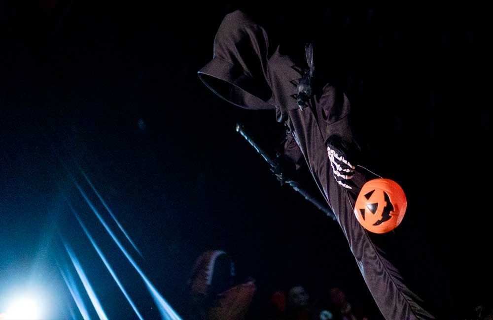 A person in a grim reaper costume is holding a pumpkin in the dark.