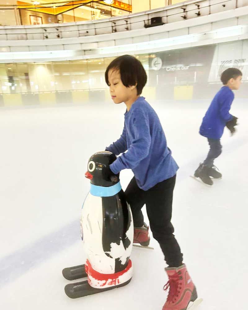 A young boy is riding on the back of a penguin statue on an ice rink.