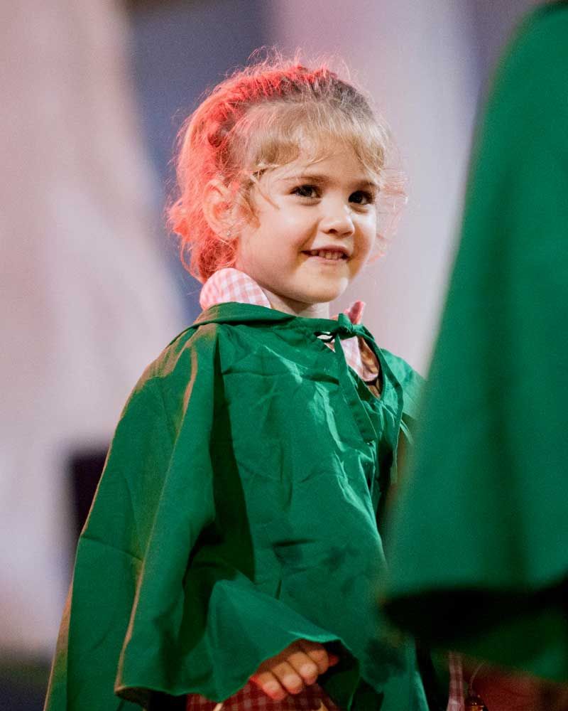 A little girl is wearing a green cape and smiling.