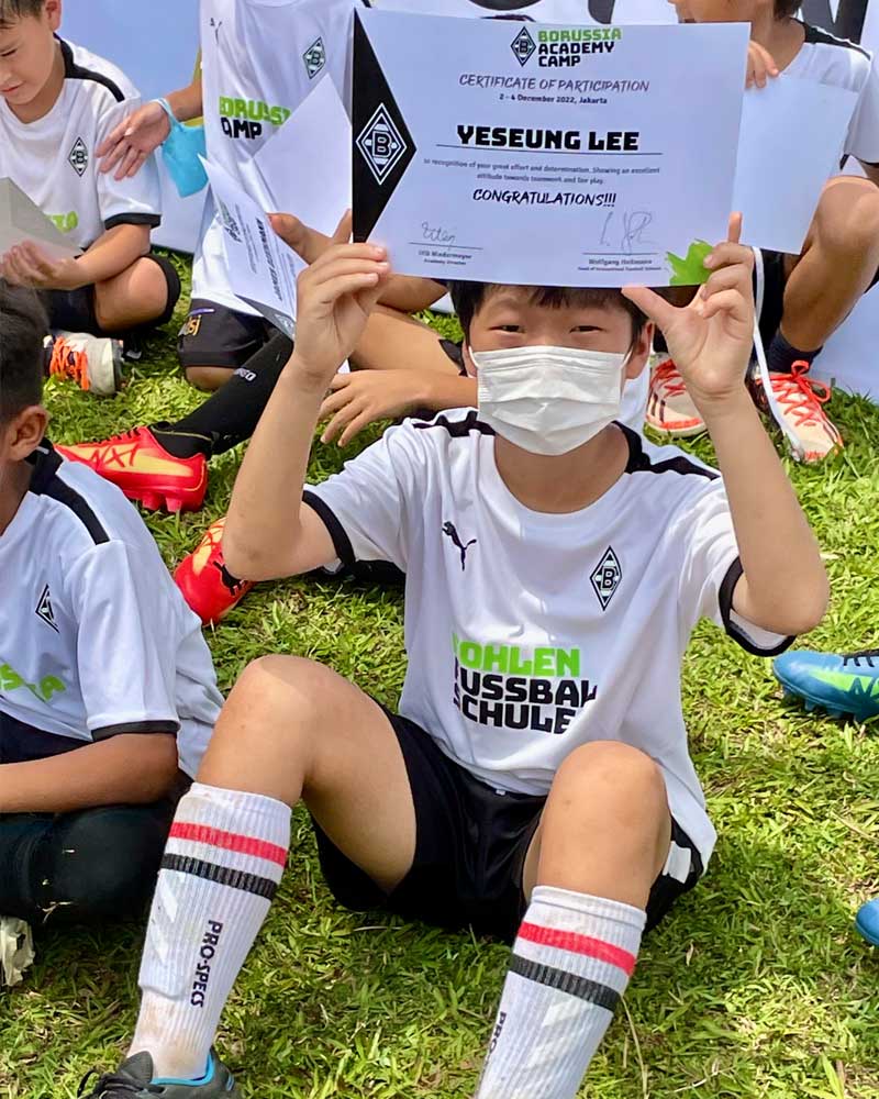 Boy in a soccer uniform holding a certificate while sitting on the grass during a sports event
