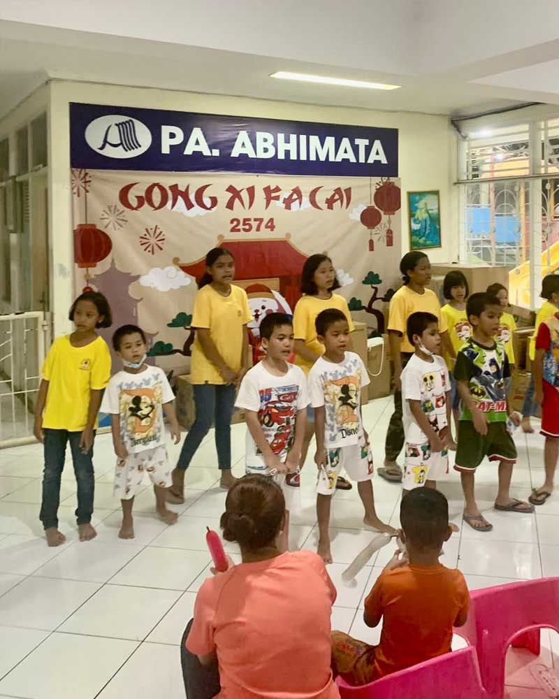 A group of children are standing in front of a sign that says pa abhimata