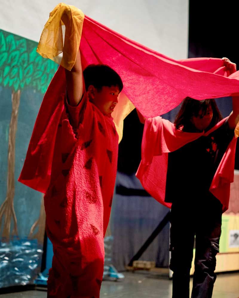 A boy and a girl are holding a red cloth over their heads