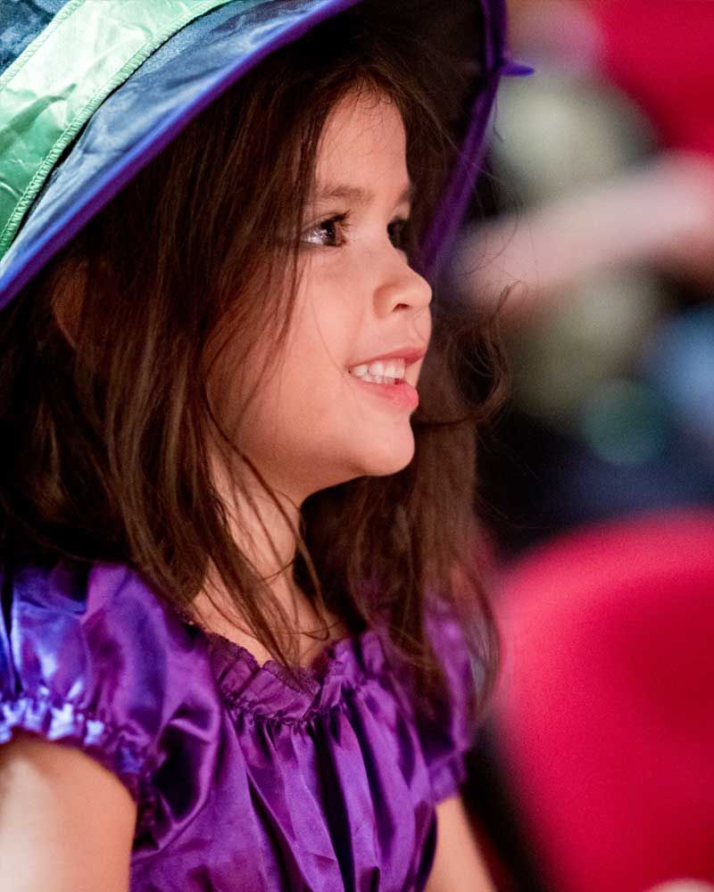 A little girl is wearing a purple dress and a hat.