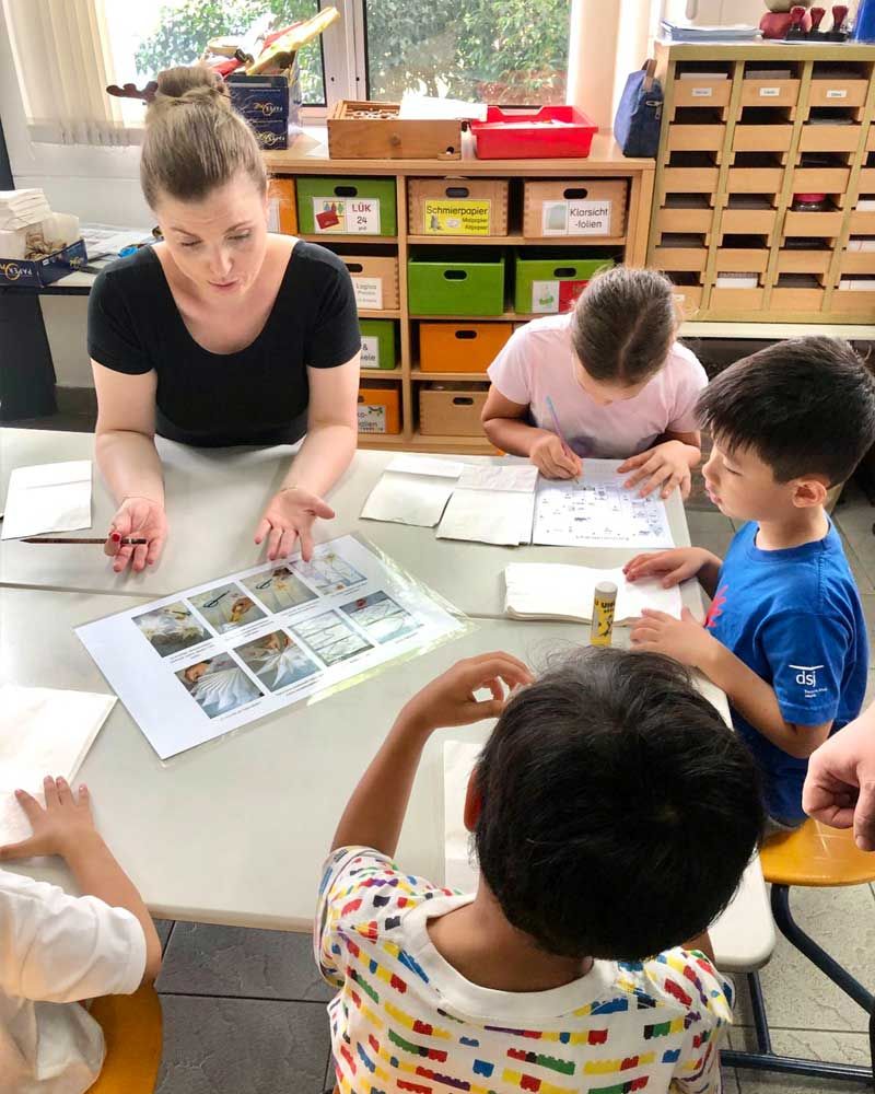 A woman is sitting at a table with a group of children.