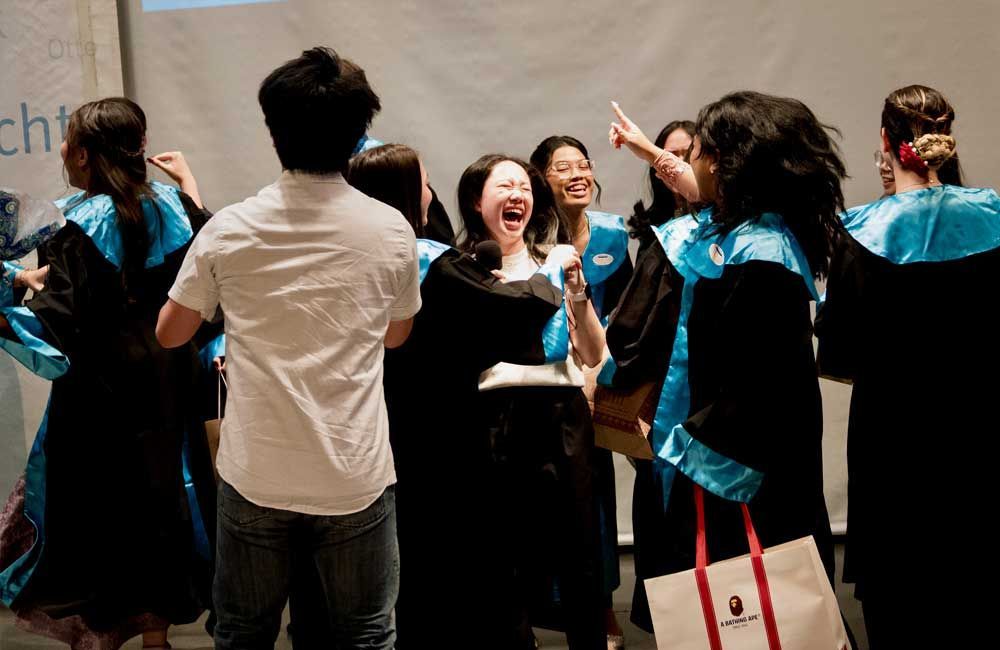 A group of people in graduation gowns are standing in a circle and laughing.