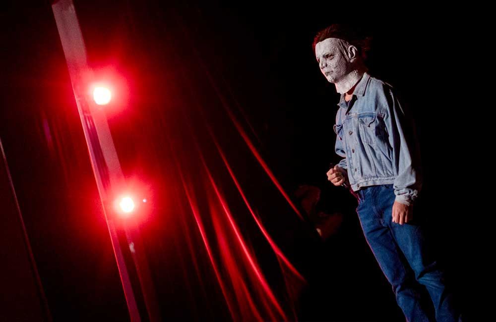 A man in a mask is standing on a stage in front of red lights.