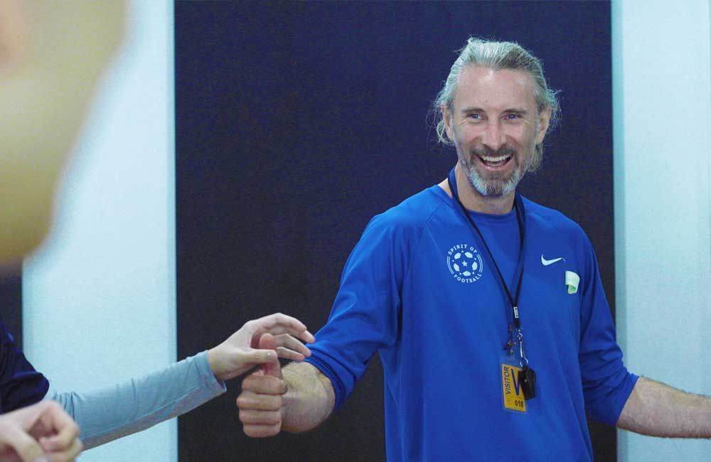 A man in a blue shirt is giving a thumbs up to a group of people.