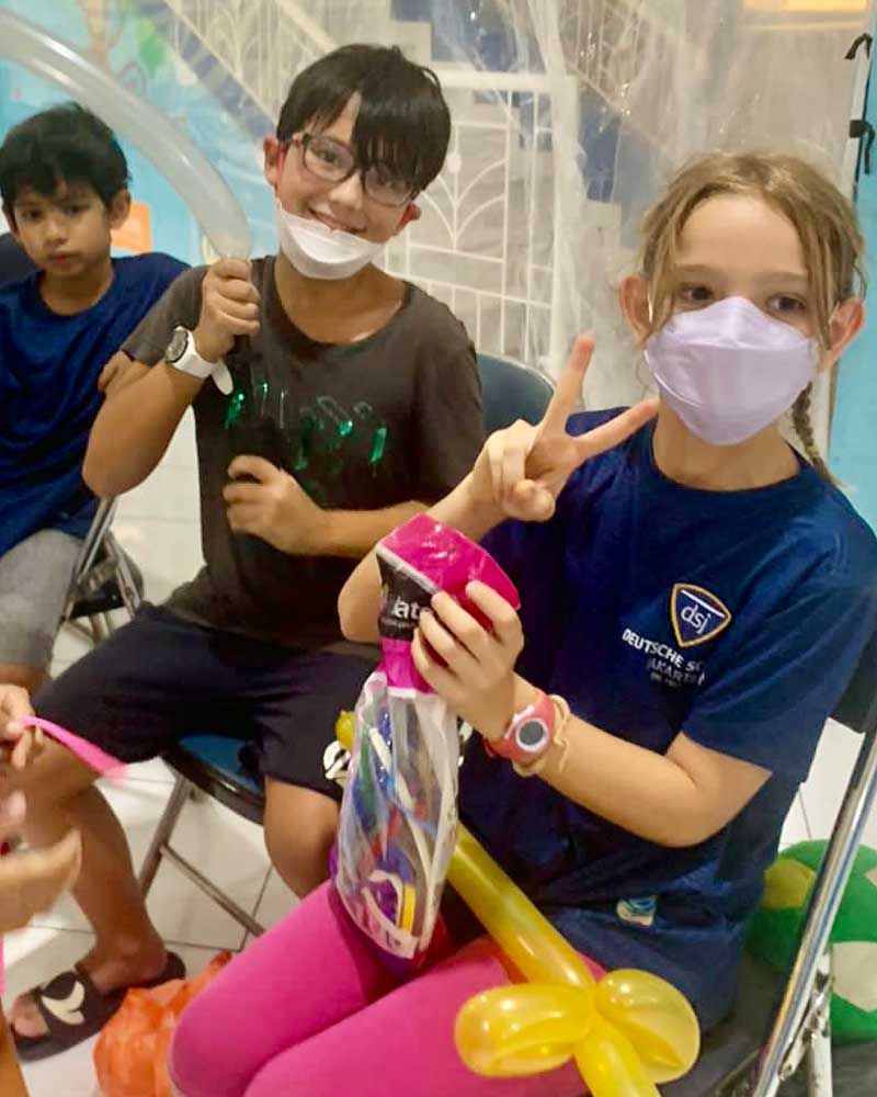 A group of children wearing face masks are sitting in chairs.