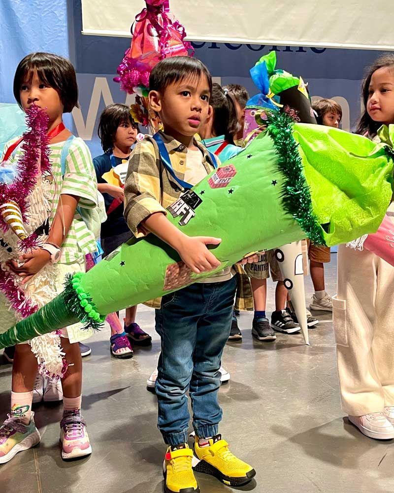 A group of children are standing in a line holding a green cone.