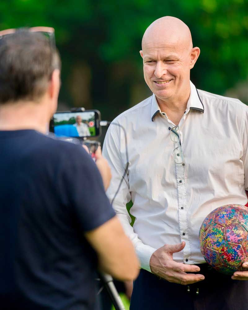 A man is holding a soccer ball and talking to another man.