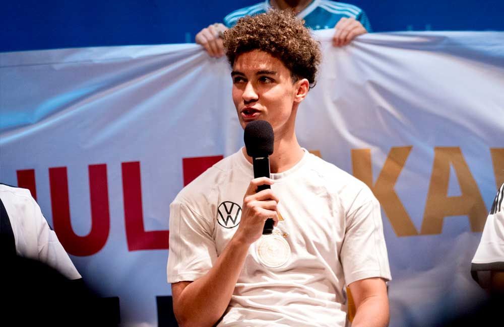 A man in a white shirt is holding a microphone and speaking into it.