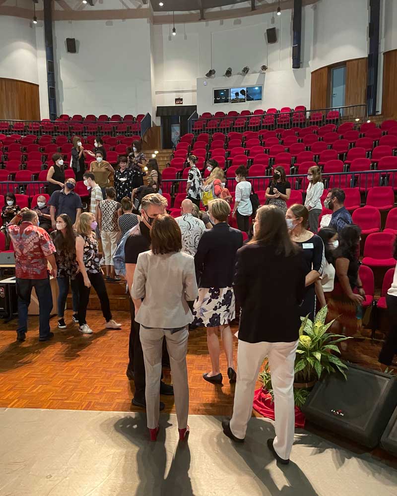 A group of people are standing in a large auditorium with red seats.