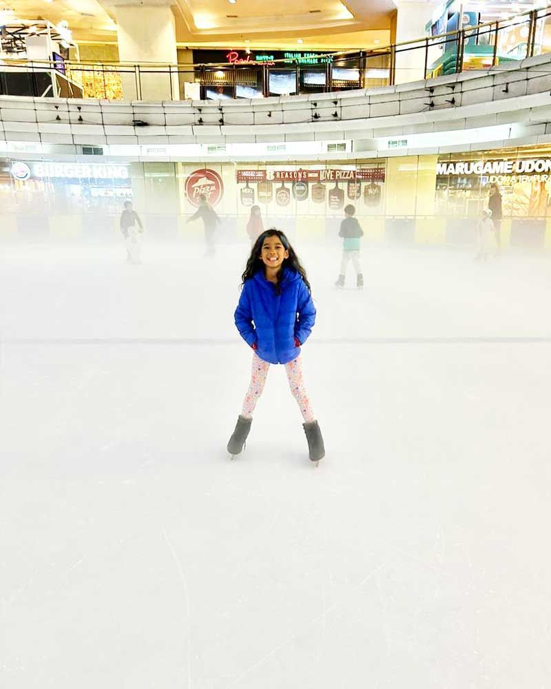 A little girl is standing on a ice rink in a mall.