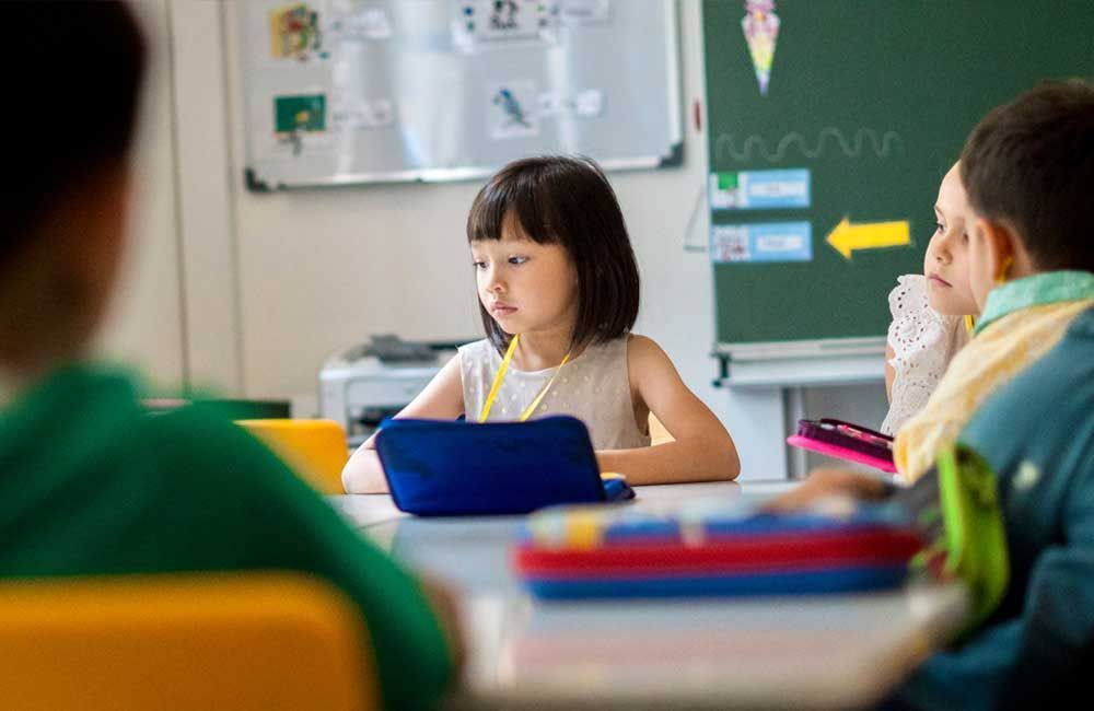A young girl is sitting at a desk in a classroom using a tablet computer.