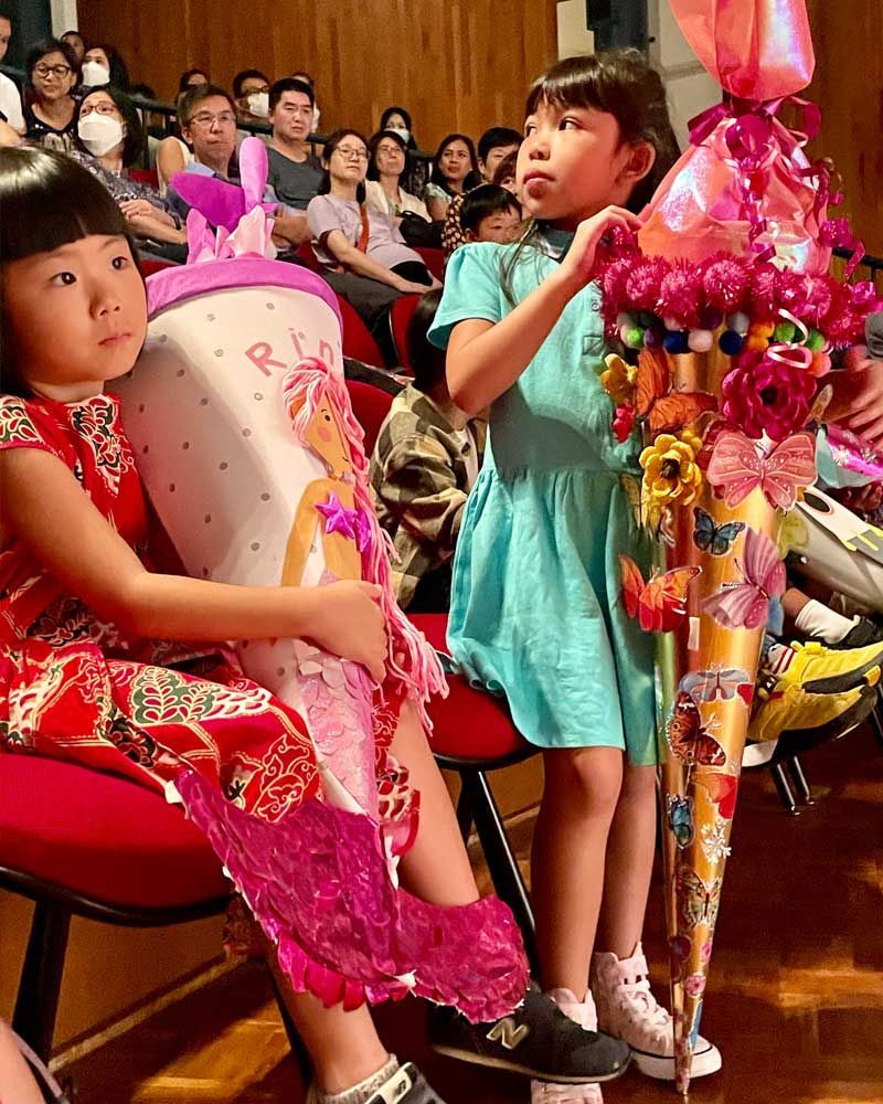 Two little girls are sitting in front of a crowd holding balloons.