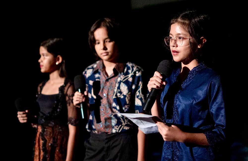 Three young girls are standing next to each other on a stage holding microphones.