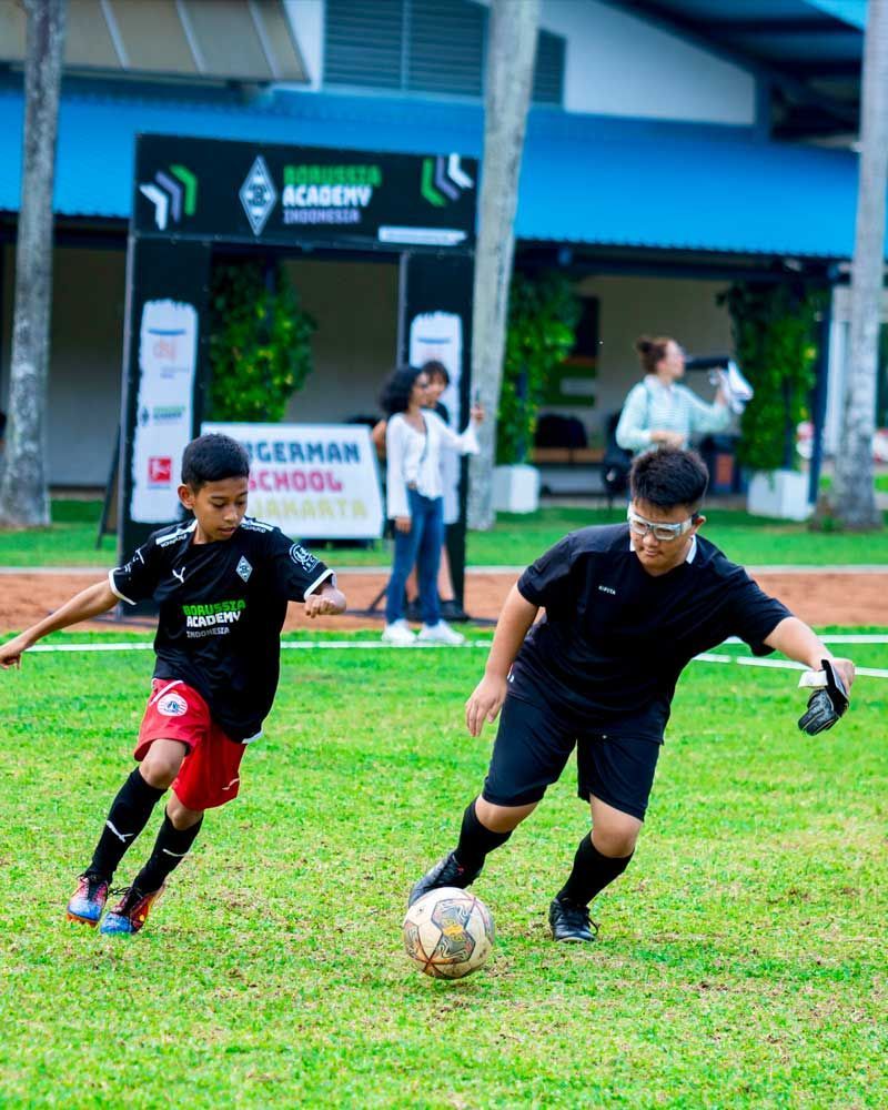 Two boys are playing soccer in front of a german school sign