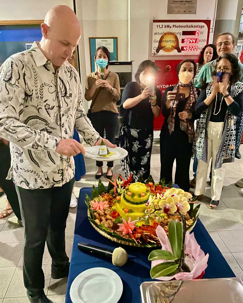 A man is cutting a cake in front of a crowd of people.