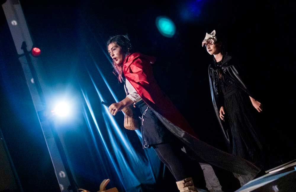 A woman in a red cape is standing on a stage next to a man in a black cape.