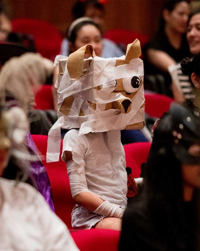 A group of people are sitting in red chairs and one of them is wearing a mummy costume