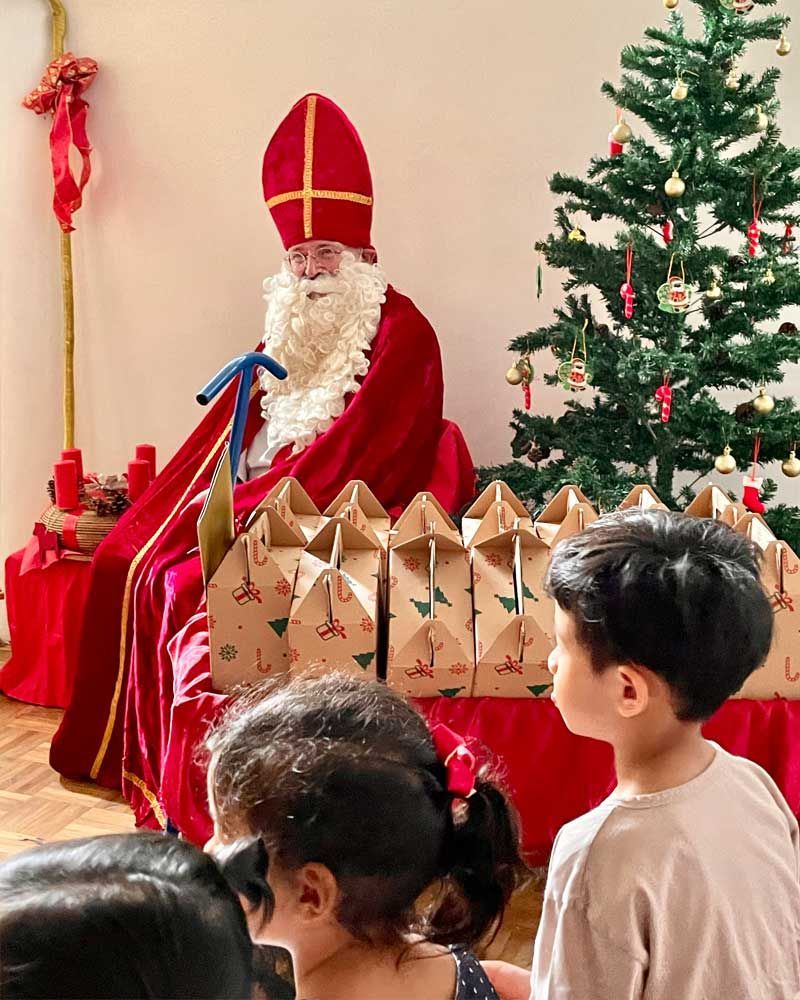A group of children are sitting in front of a christmas tree looking at santa claus