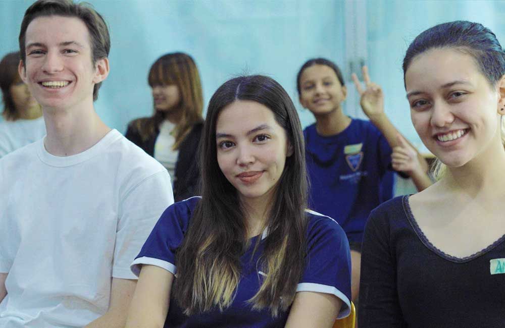 A group of young people are sitting in a classroom and smiling for the camera.