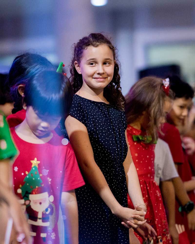 A girl in a black dress is standing in a line with other children.