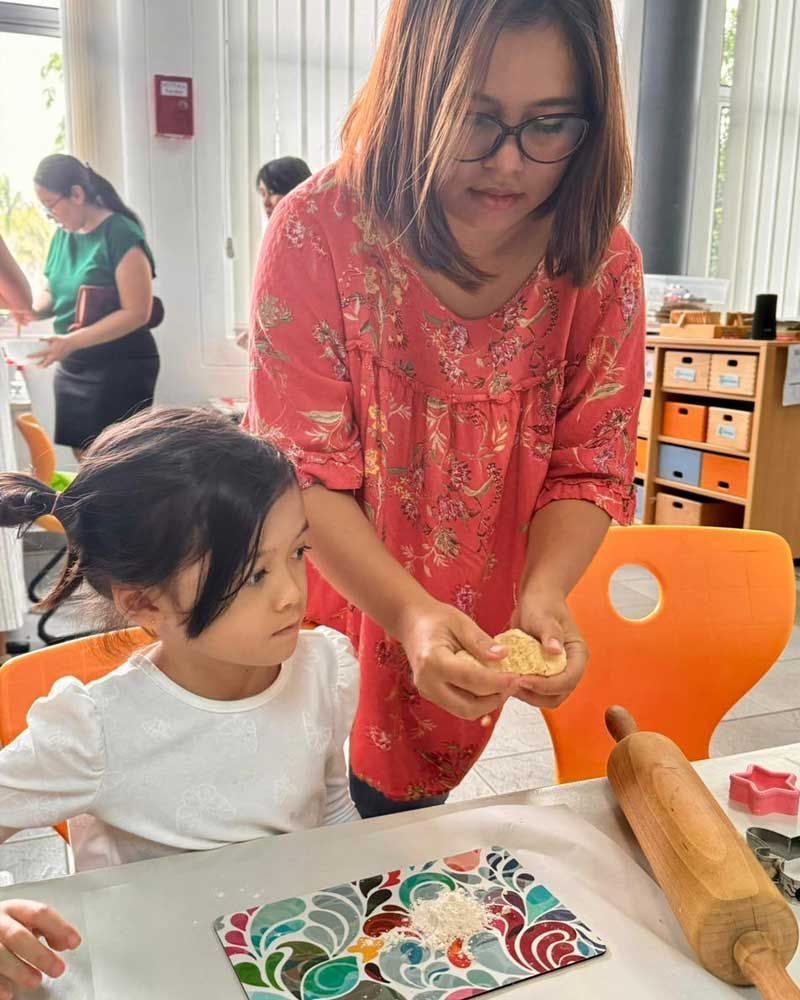 A woman is helping a little girl roll out dough with a rolling pin.