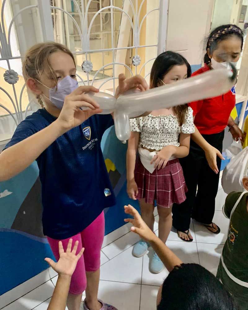A group of children wearing face masks are playing with balloons.