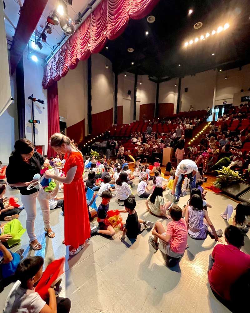 A group of children are sitting on the floor in a large auditorium